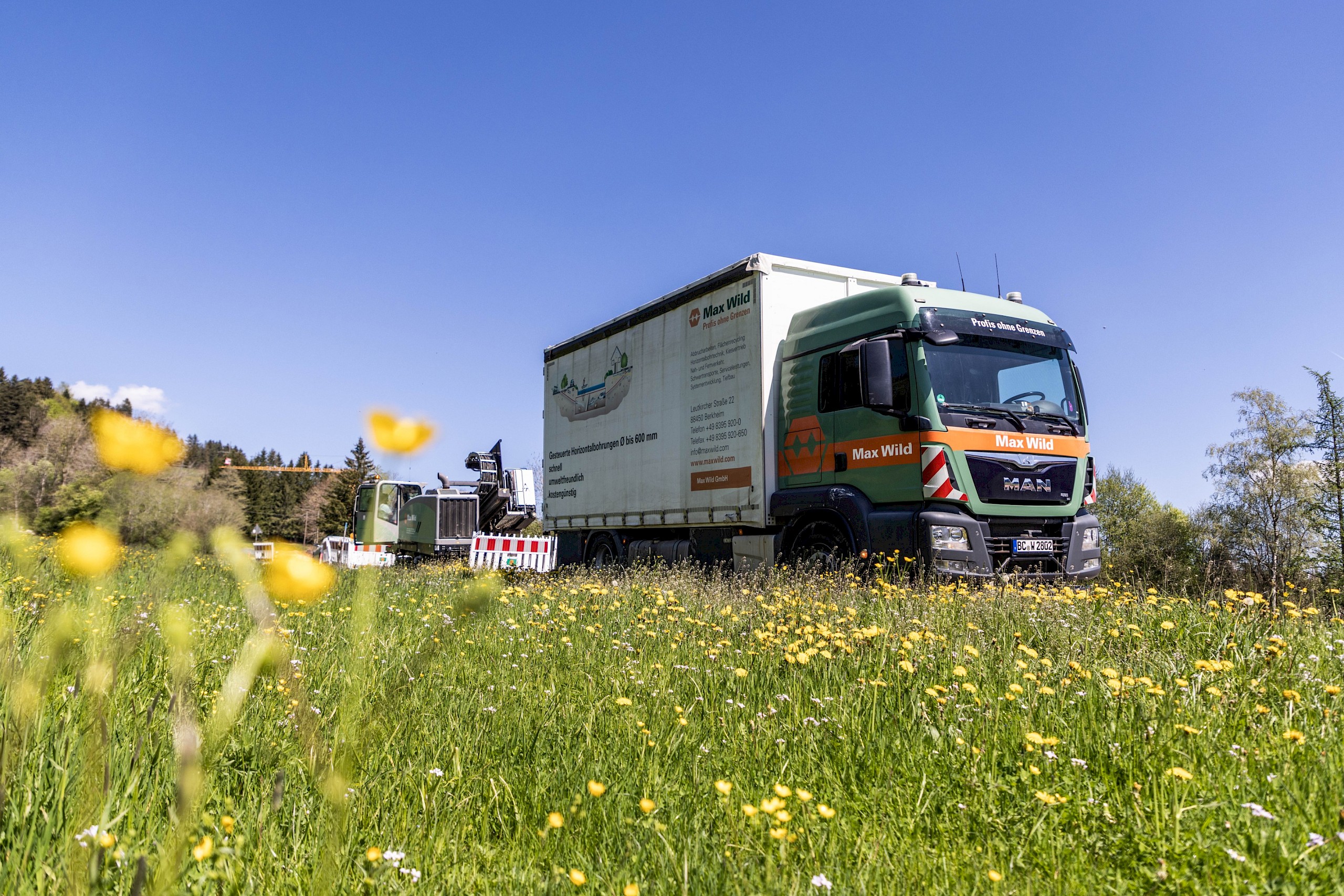 Ein Lastwagen von best wood Schneider steht auf einer blühenden Wiese unter blauem Himmel. Auf dem LKW ist Werbung für Holzpellets zu sehen.