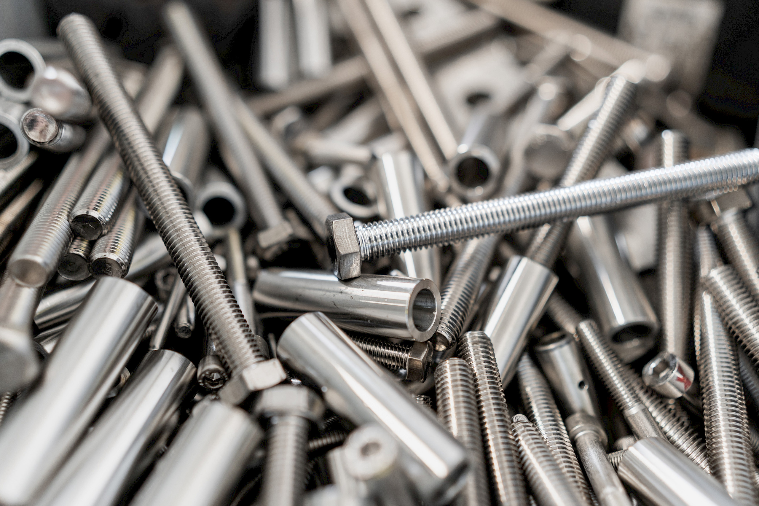 Stapel von silbernen Schrauben, Muttern und Metallzylindern.